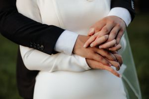 Close-up of hands with wedding rings clasped together in an intimate moment.