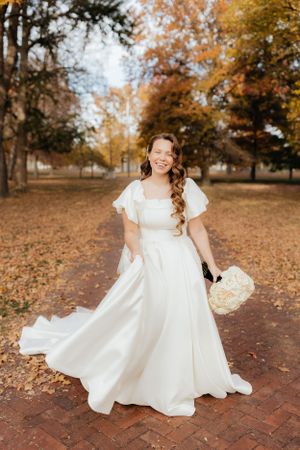 A flowing white wedding dress twirls gracefully among autumn leaves on a brick pathway.