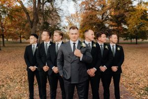 Groomsmen in black suits share laughs during outdoor fall photo session.