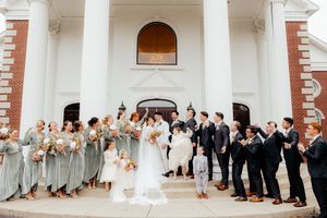 Wedding party lined up outside a white columned building with bridesmaids in gray and groomsmen in dark suits.