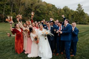 Wedding party poses outdoors with bridesmaids in rust-colored dresses and groomsmen in navy suits.
