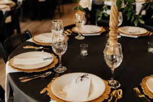Elegant table settings with gold cutlery and crystal glasses on black tablecloths.