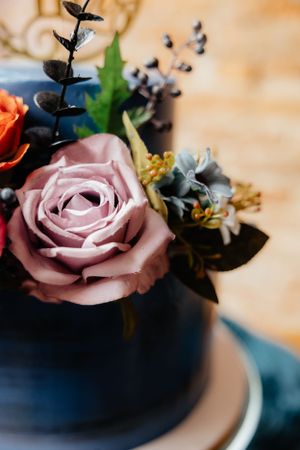 Close-up of delicate pink roses and floral decorations on a navy blue wedding cake.
