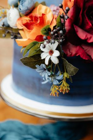 Detailed shot of orange and burgundy flowers with white accents adorning a wedding cake.