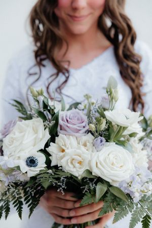 Elegant bridal bouquet featuring white roses, anemones, and lavender flowers.