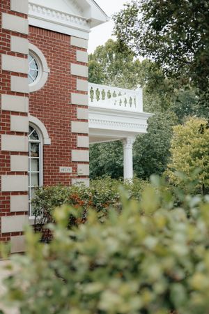 Elegant red brick building with white trim and architectural details surrounded by greenery.