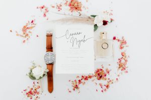 Wedding invitation flatlay with watch, flowers and pink petals on white background.
