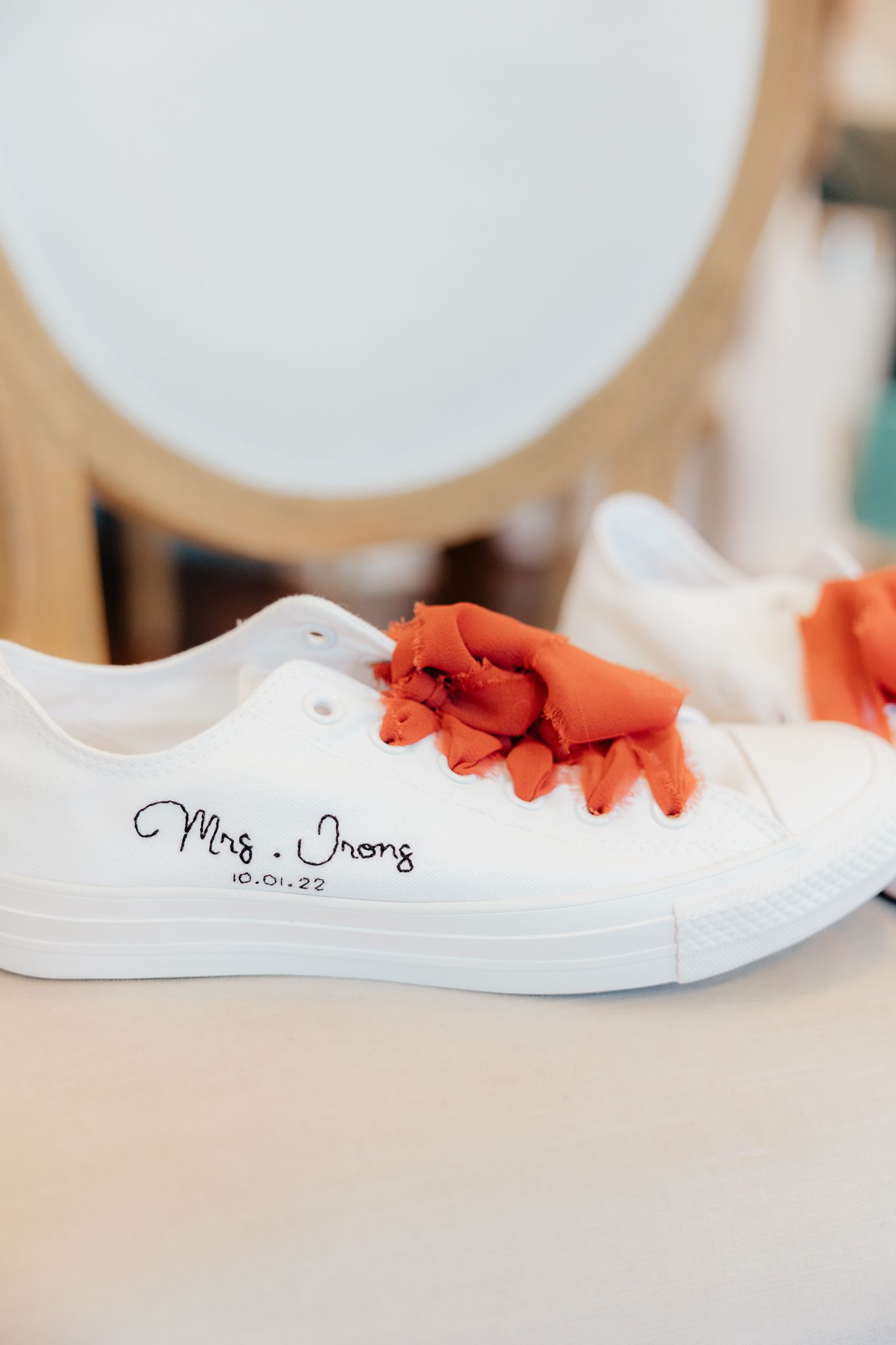White wedding sneakers with orange ribbons and personalized writing.