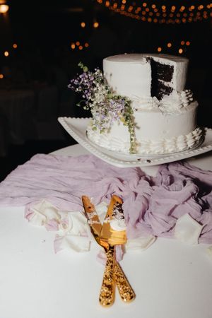 Elegant white wedding cake decorated with delicate flowers and gold serving utensils.