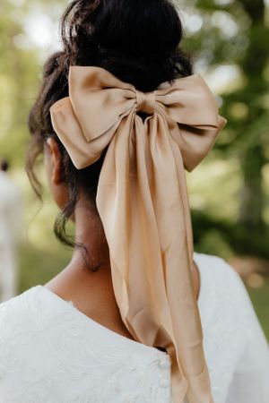 Close-up of champagne colored silk bow hair accessory on wedding dress.