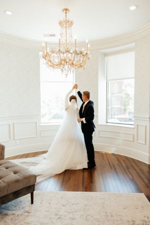 Elegant white room with chandelier and hardwood floors featuring a wedding dress display.