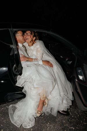 Bride in white wedding dress getting into a car at night.
