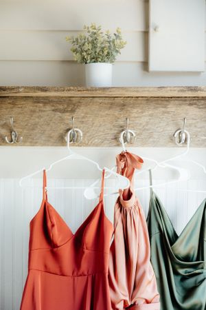 Wedding party dresses in coral and sage green hanging on rustic wooden hooks.