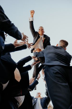 Business team celebrating success with hands raised against bright background.