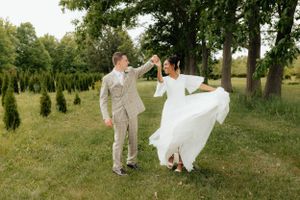 Couple dancing and twirling in wedding attire on grassy field.