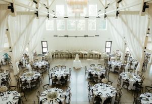 Elegant white wedding reception venue with round tables and draped fabric decor.