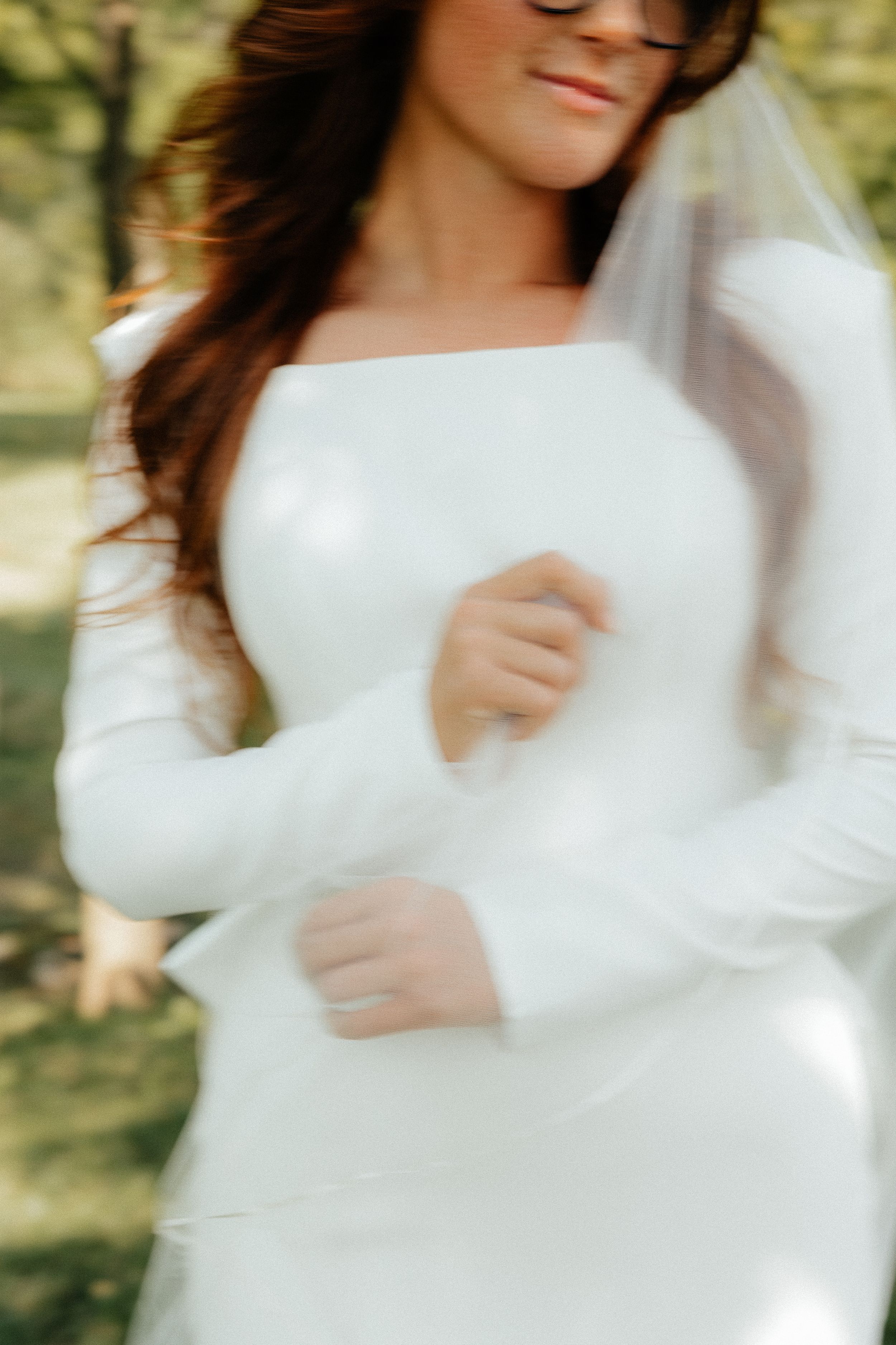 Artistic blurred portrait of bride in long-sleeved white wedding gown.
