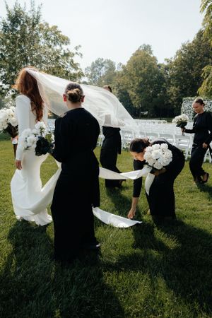 Wedding party in black and white attire helping with dress arrangements outdoors.