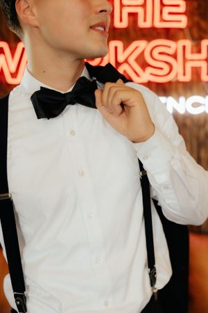 Formal attire detail with white shirt, bow tie, and suspenders against neon lighting.