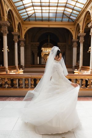 A flowing white wedding dress twirls gracefully in an ornate hall with skylights and architectural details.