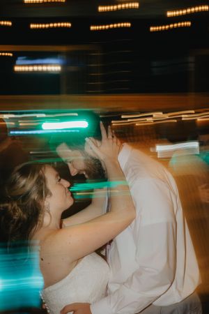 A couple shares a romantic dance moment with motion blur and colorful lighting at a wedding reception.