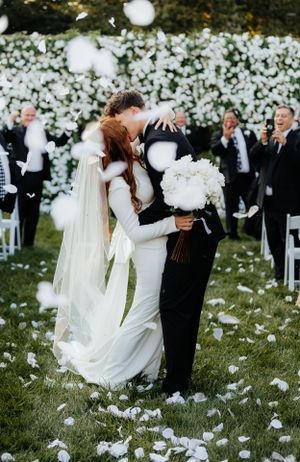 White flower petals float through the air during a joyful outdoor wedding celebration.