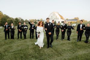 Wedding party in formal attire poses on a grassy field during golden hour.