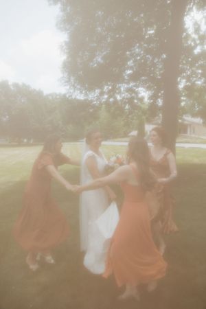 Ethereal outdoor scene with people in rust-colored and white dresses dancing in sunlight.