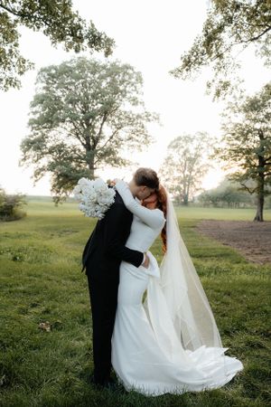 Newlyweds share a romantic moment on a grassy hillside during sunset.
