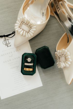 Wedding accessories including ivory heels, rings, and jewelry boxes on a light surface.