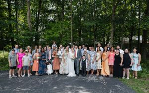 Large group wedding photo of guests and wedding party gathered outdoors in a wooded setting.