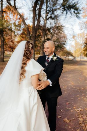 Autumn wedding scene with fallen leaves on ground and trees in background.