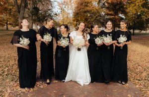 Wedding party in black attire poses against a backdrop of fall foliage.