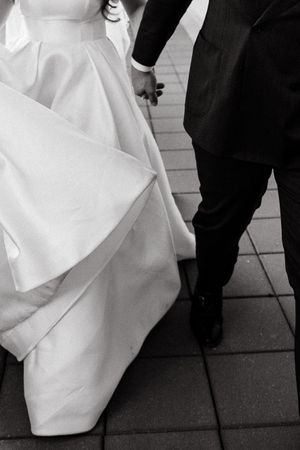 Close-up of white wedding dress hem against stone pavement in black and white.