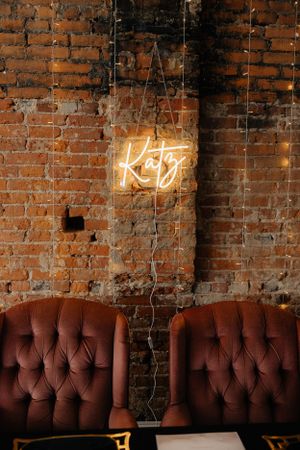 Vintage brown leather tufted couch against brick wall with neon lights creating moody atmosphere.