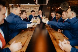 Groomsmen in navy suits sitting at a rustic wooden bar.