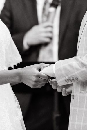 Black and white close-up of hands exchanging wedding rings during ceremony.