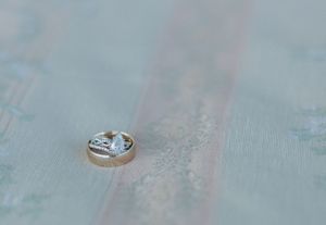 Close-up view of elegant engagement and wedding rings on a light blue textured surface.