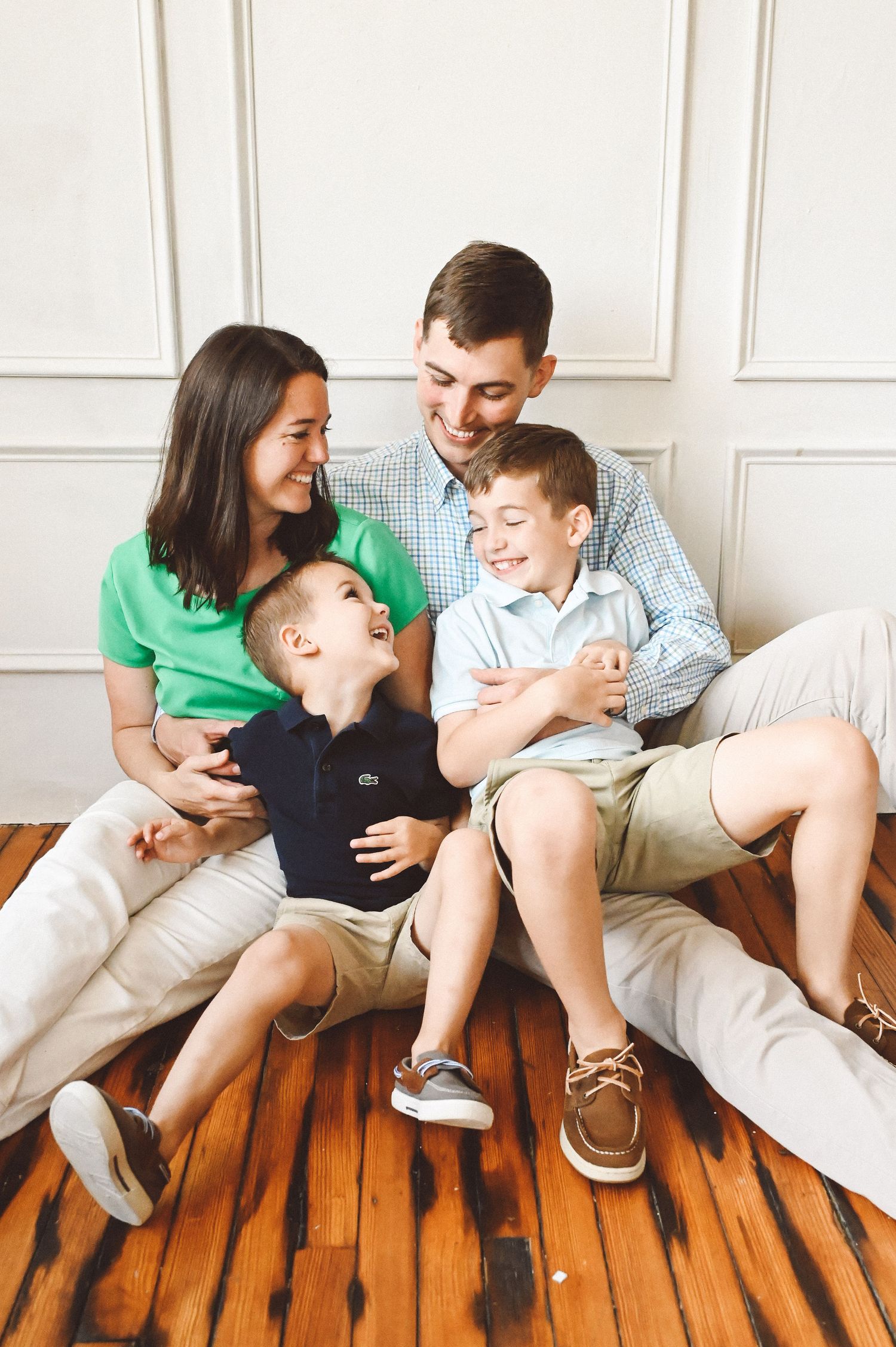 Happy family laughing together while sitting on wooden floor at home.
