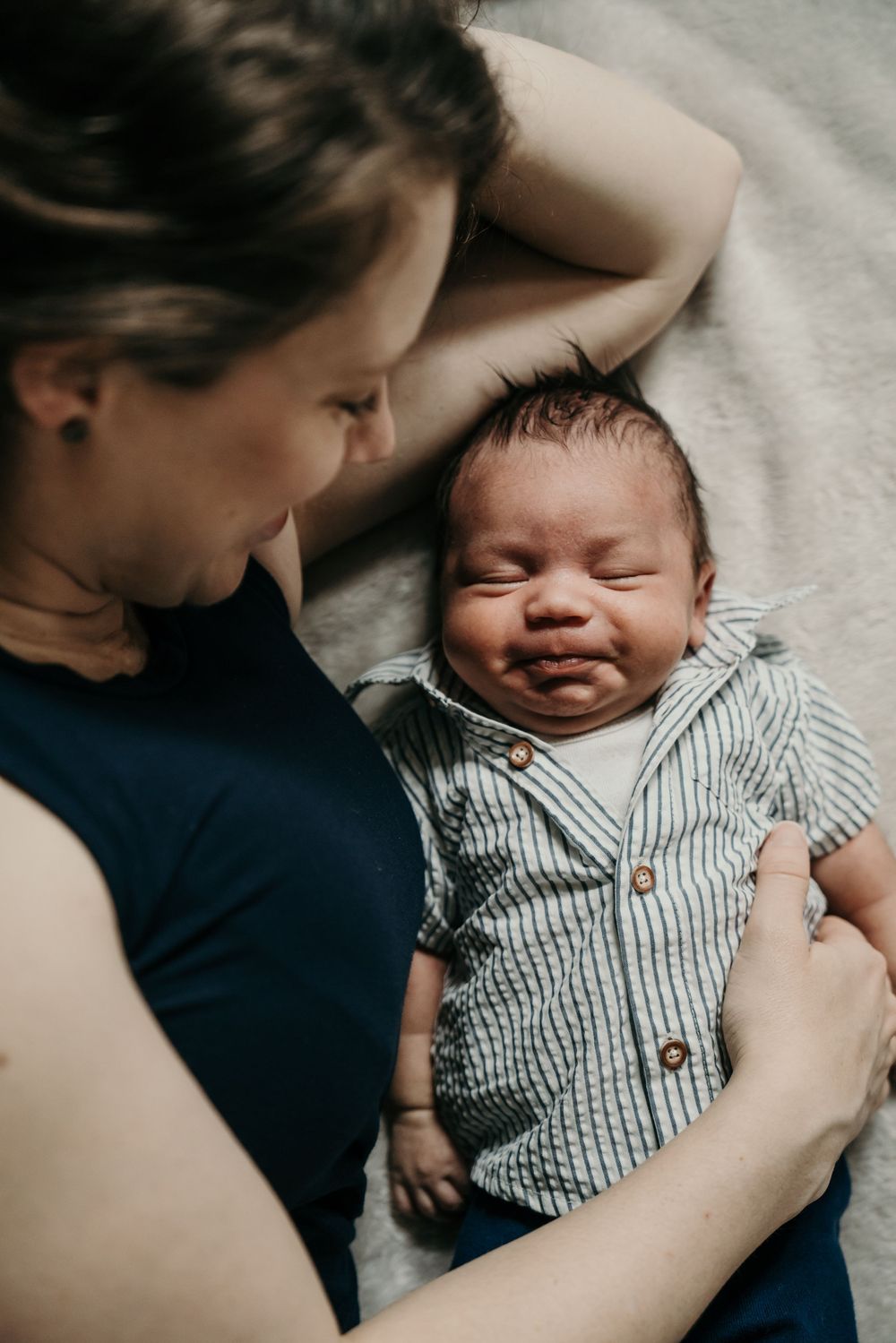 Tender moment between parent and newborn baby wearing striped shirt on soft gray blanket.