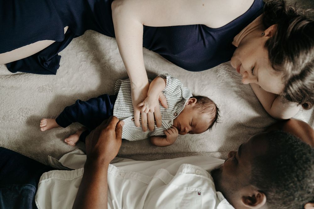 Intimate moment with newborn baby wearing gray shirt laying between loved ones.