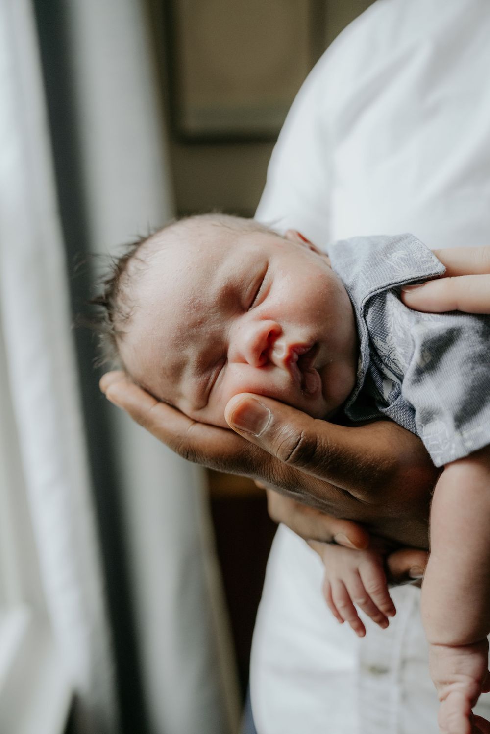 Sleeping newborn baby in gray outfit being tenderly cradled.