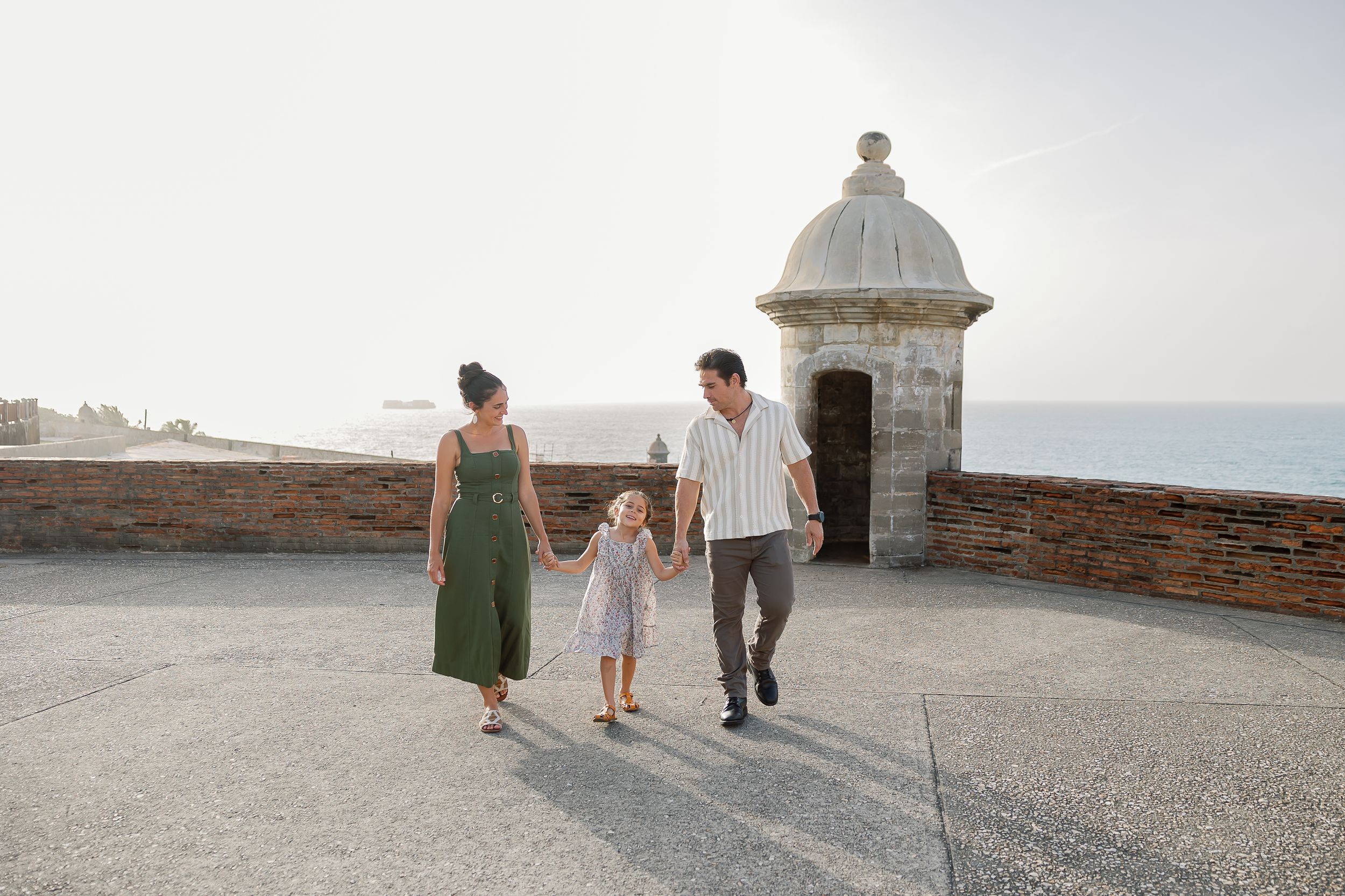 A family walking along a stone wall with a small tower in the background.