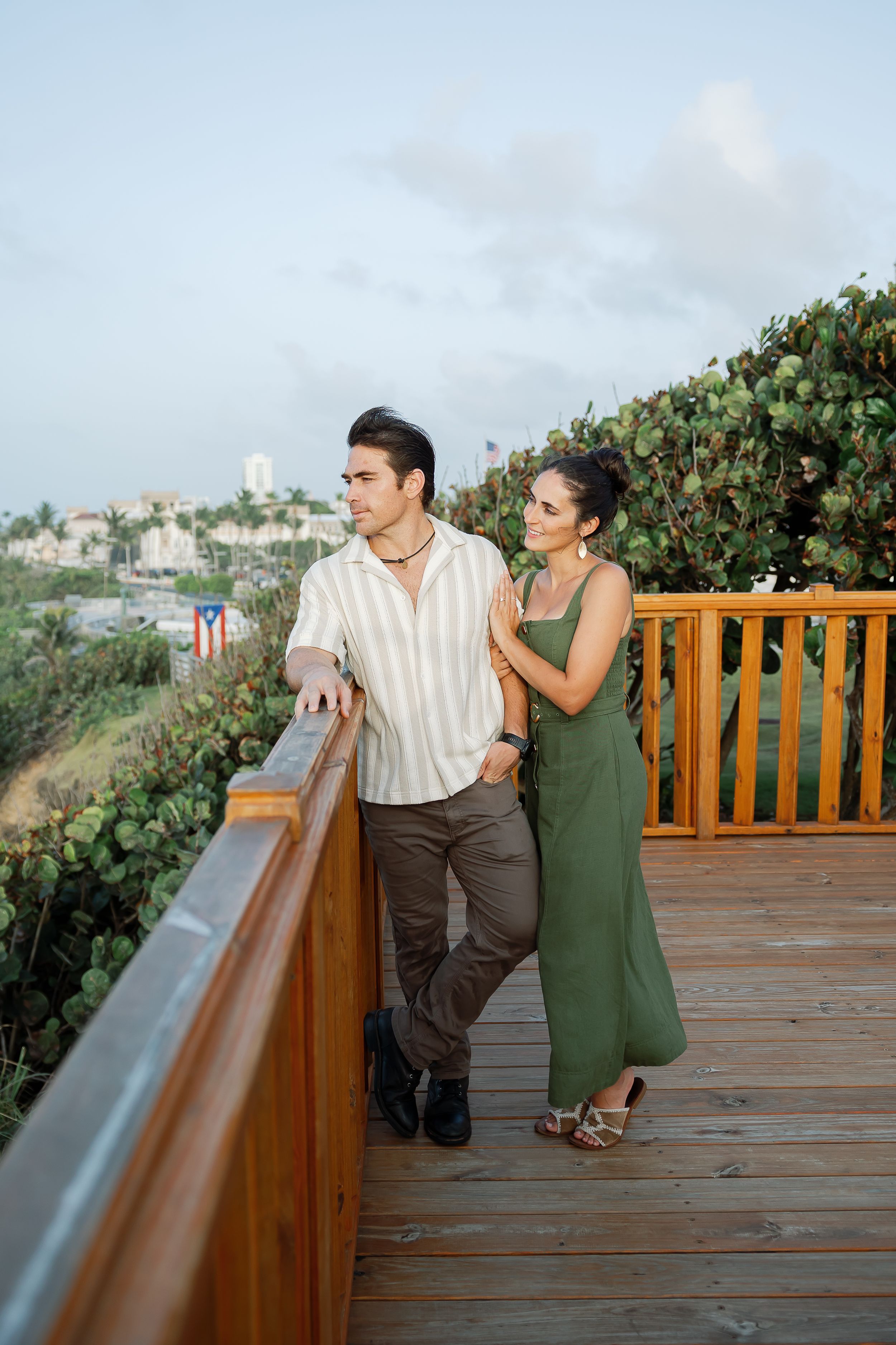 A couple stands on a wooden deck overlooking a scenic landscape.