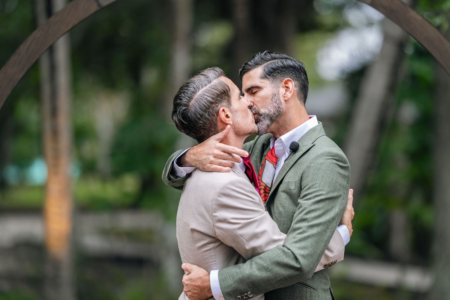 Bride and groom kiss passionately after ceremony holding a large pink floral bouquet.