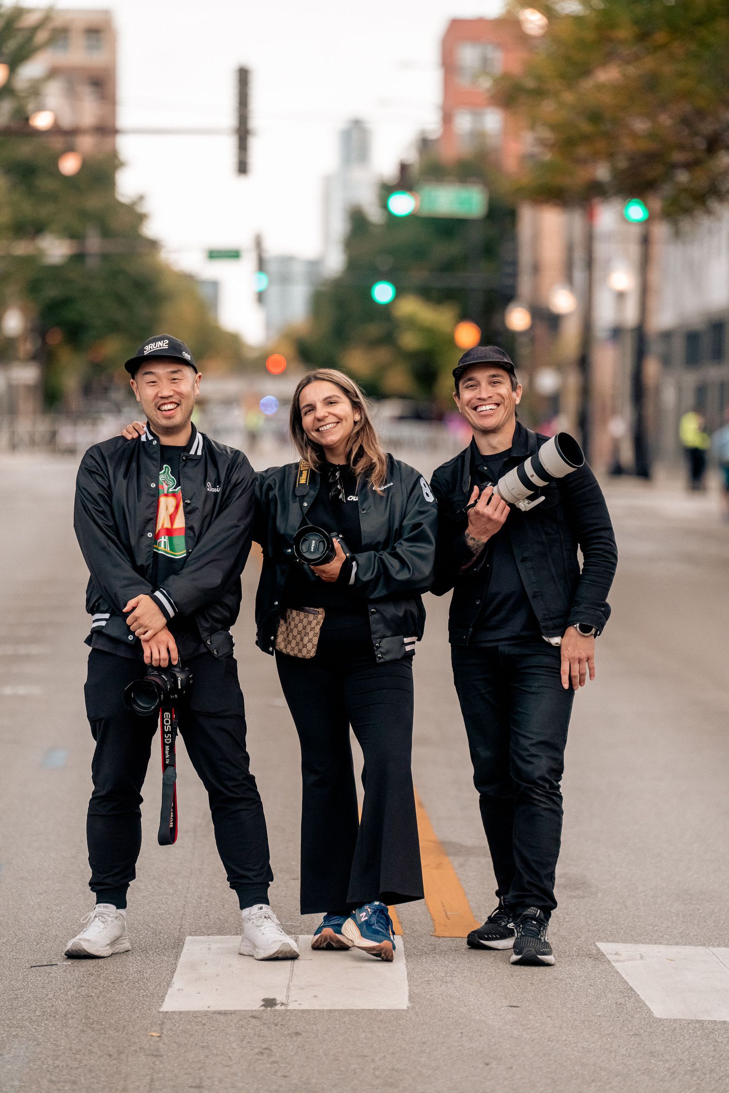 Three professional photographers standing together on a city street with cameras and lenses, ready for a photo shoot.