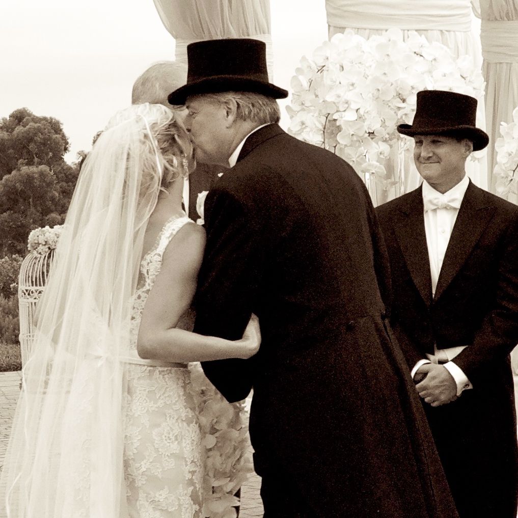 A sepia-toned wedding moment captured during a traditional ceremony with top-hatted men and a bride in white veil.  Pellican Hill, Newport.