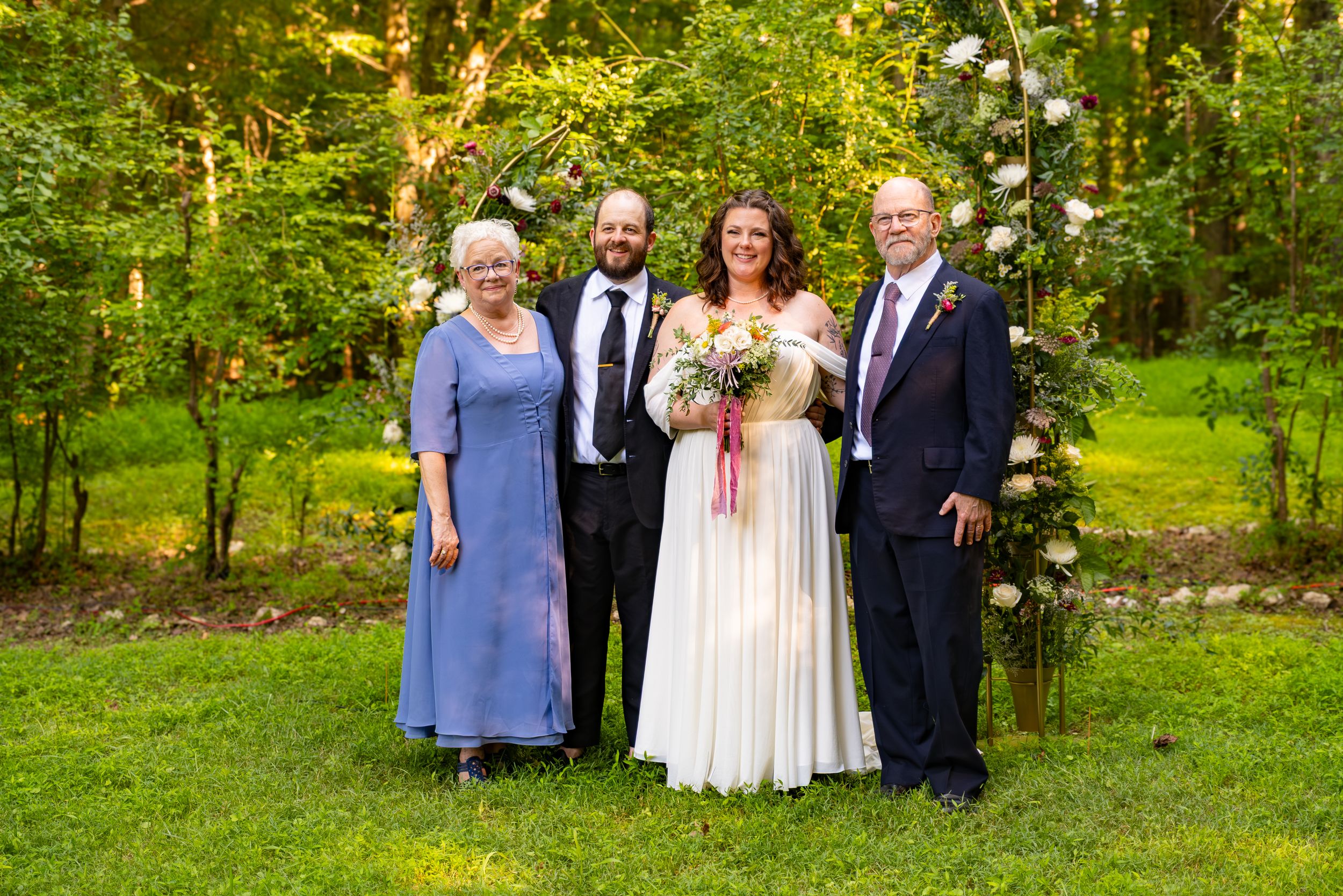 The wedding party poses together outdoors for formal photos in a scenic green garden setting. Bill Griffin Photography.
