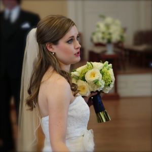 Bride in strapless lace wedding dress holding yellow and white floral bouquet during indoor ceremony.