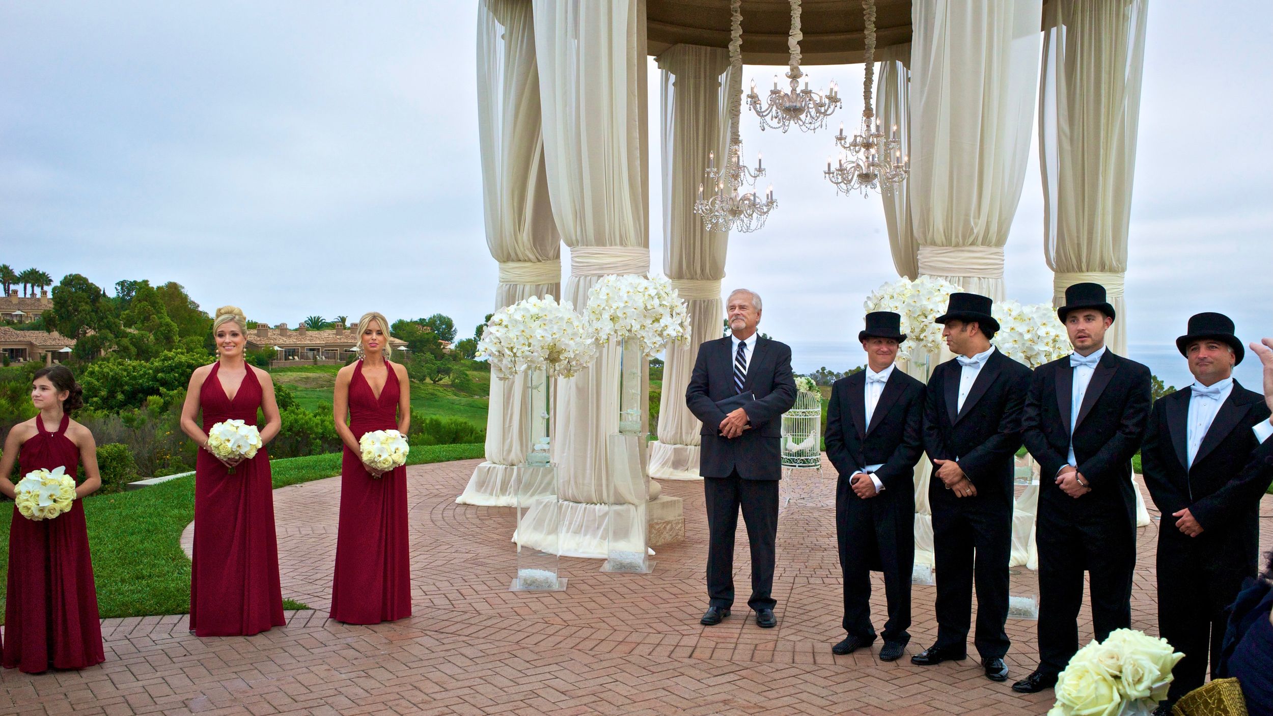 A panoramic view of a wedding party standing in an elegant white gazebo with red and navy color accents.  Newport, CA.